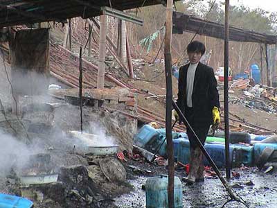 A man in Guiyu, China, heats a combination of nitric and hydrochloric acid, while inhaling acid fumes, chlorine and sulfur dioxide, without respiratory protection. Leftover acids and sludge are dumped in the river.