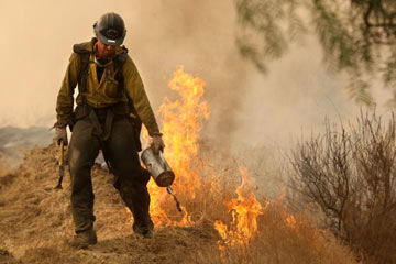 A U.S. Forest Service hotshot uses a drip torch to light a backfire. A drip torch dribbles and ignites fuel (usually either diesel or stove oil) at the pull of a trigger.