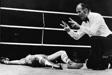 A boxing referee administers the count.